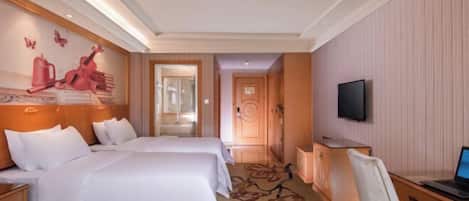 A hotel room with two beds, a desk with a computer, a television, and a shower area.