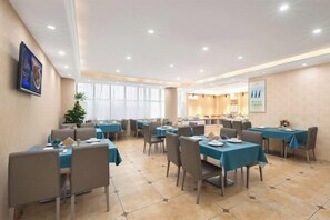 A hotel dining area with multiple tables and chairs, a large window, and a reception desk. - Vienna Hotel (Dongguan Dalang) (Dongguan)