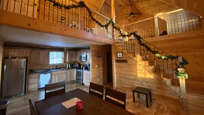 Interior espacioso de una cabaña de troncos, con cocina, comedor y una escalera con barandilla.