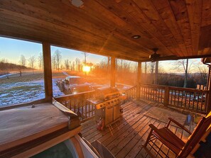 Une terrasse en bois avec un barbecue et une chaise, donnant sur un paysage enneigé où l’on aperçoit un véhicule et des arbres.