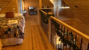 Un dormitorio acogedor en el ático, con pisos de madera, una cama con manta escocesa, un candelabro y un balcón con barandilla.