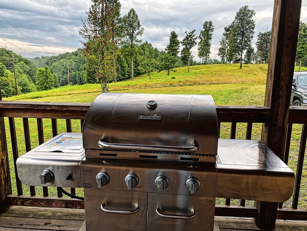 Un barbecue à gaz Char-Broil doté de quatre brûleurs, d’un thermomètre et d’un brûleur latéral, installé sur une terrasse en bois offrant une vue sur une colline verdoyante et des arbres.