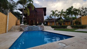 Una piscina con cubierta de piedra, rodeada de palmeras y una casa de madera.