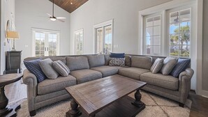 Ein geräumiges Wohnzimmer mit einer großen Eckcouch, einem Holztisch und einem Deckenventilator.