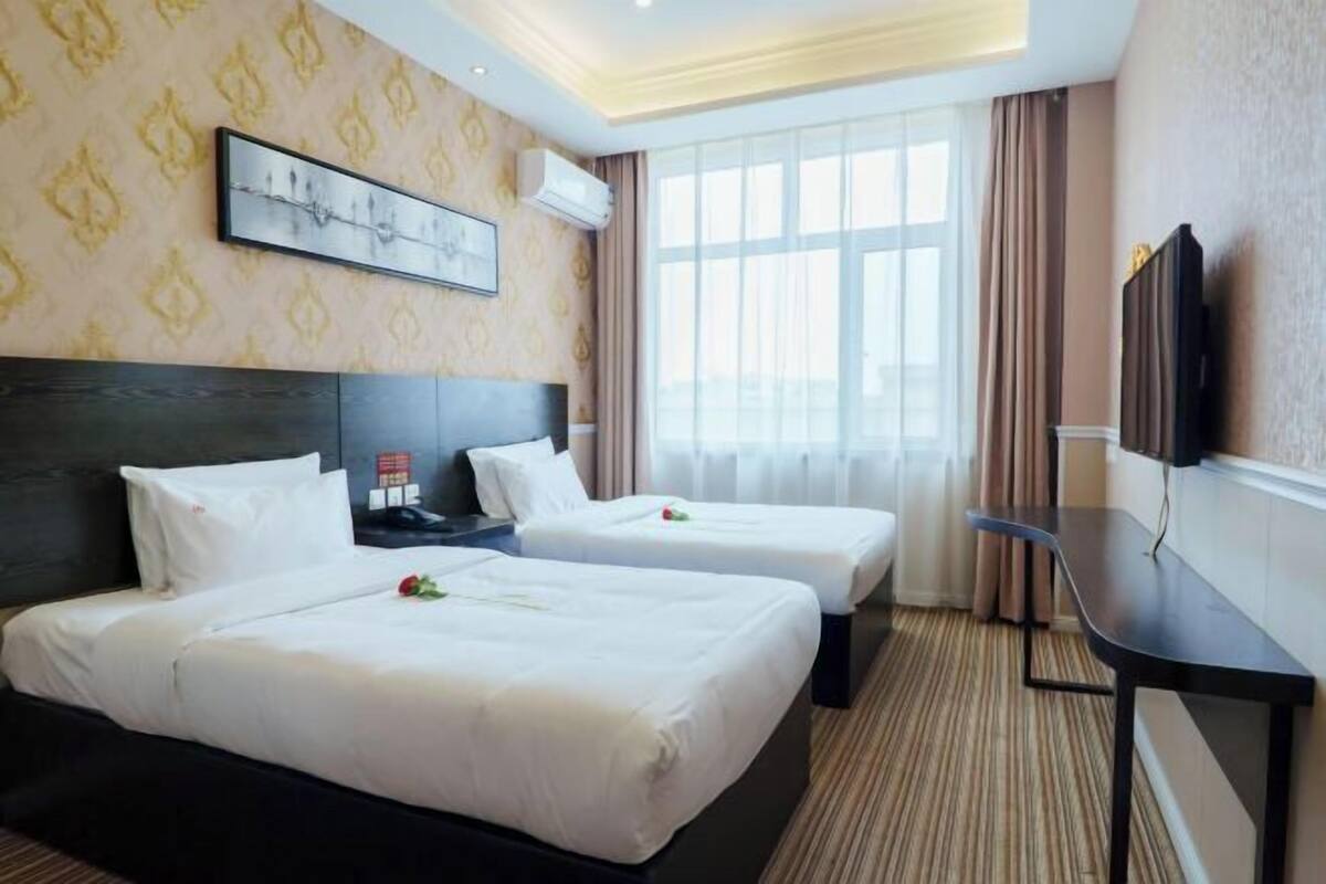 Habitación de hotel con dos camas, un escritorio, un televisor y un ventanal grande.