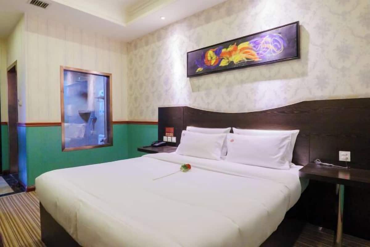 Una habitación de hotel con una cama grande, una mesita de noche, un cuadro en la pared y una ventana con vistas.