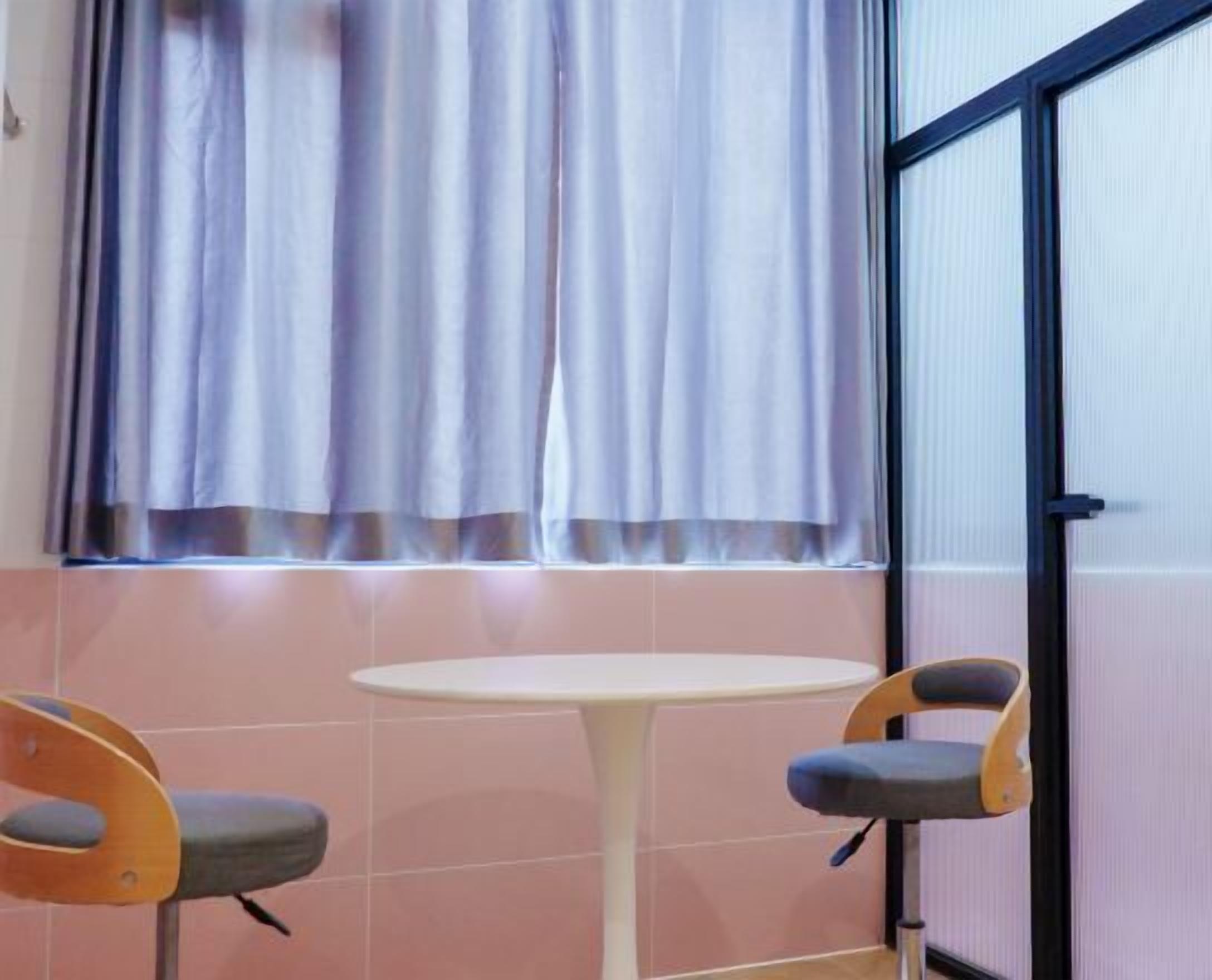 Una habitación con una pequeña mesa redonda y dos sillas, una ventana con cortinas y una puerta con marco negro.