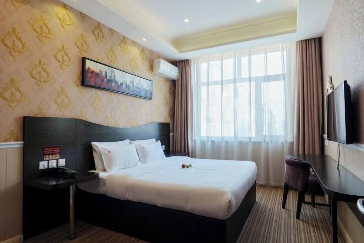 Habitación de hotel con una cama grande, un escritorio, una silla, un televisor y una fotografía de la ciudad en la pared.