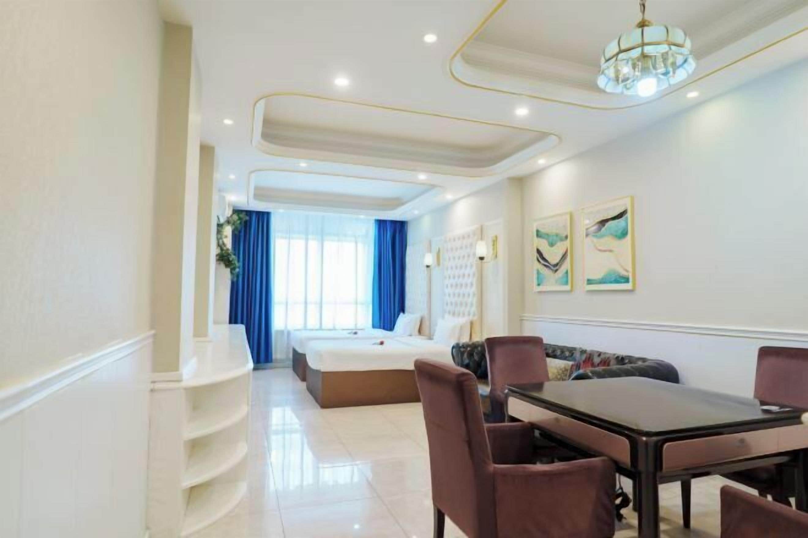 A hotel room with a bed, a dining table with chairs, a chandelier, and artwork on the wall.