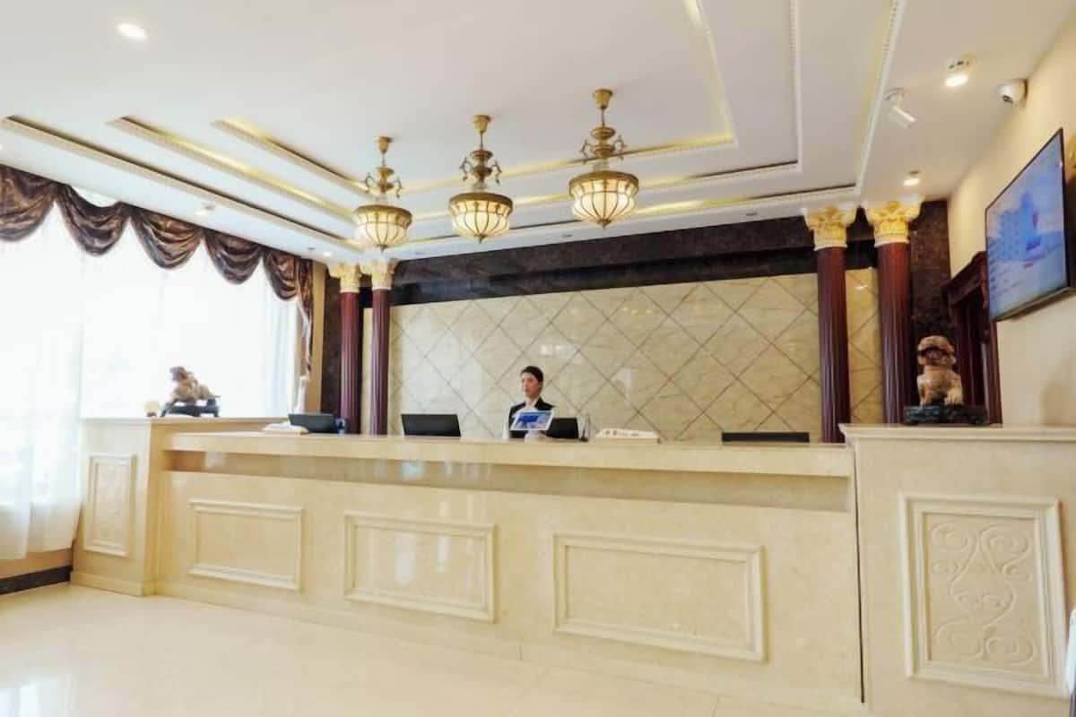 A reception desk with a marble counter, a receptionist, and a large window with curtains.