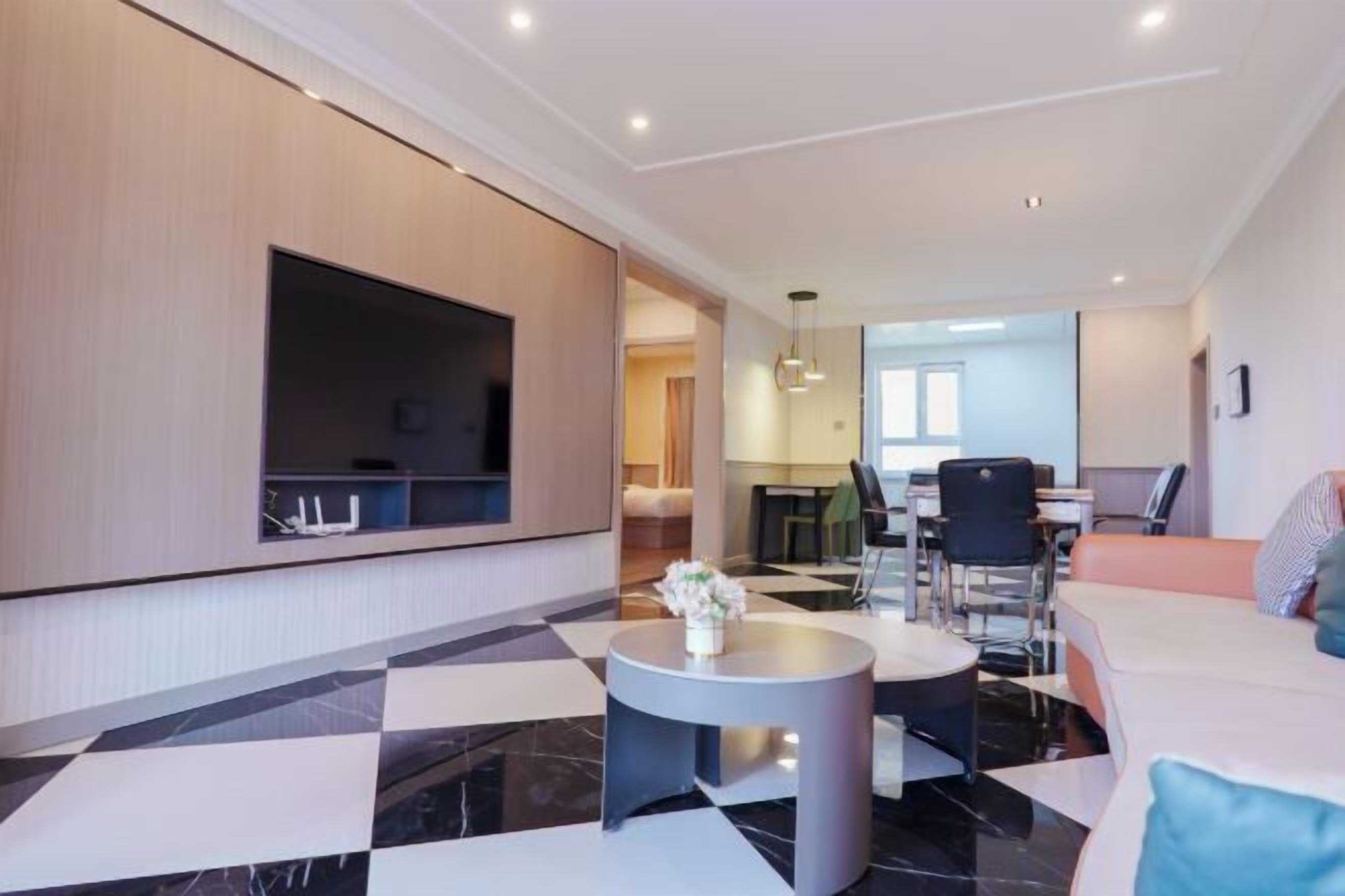 Eine moderne Hotelhalle mit einem Flachbildfernseher, einem runden Couchtisch mit Blumen, einem Essbereich mit Stühlen und einem Sofa.