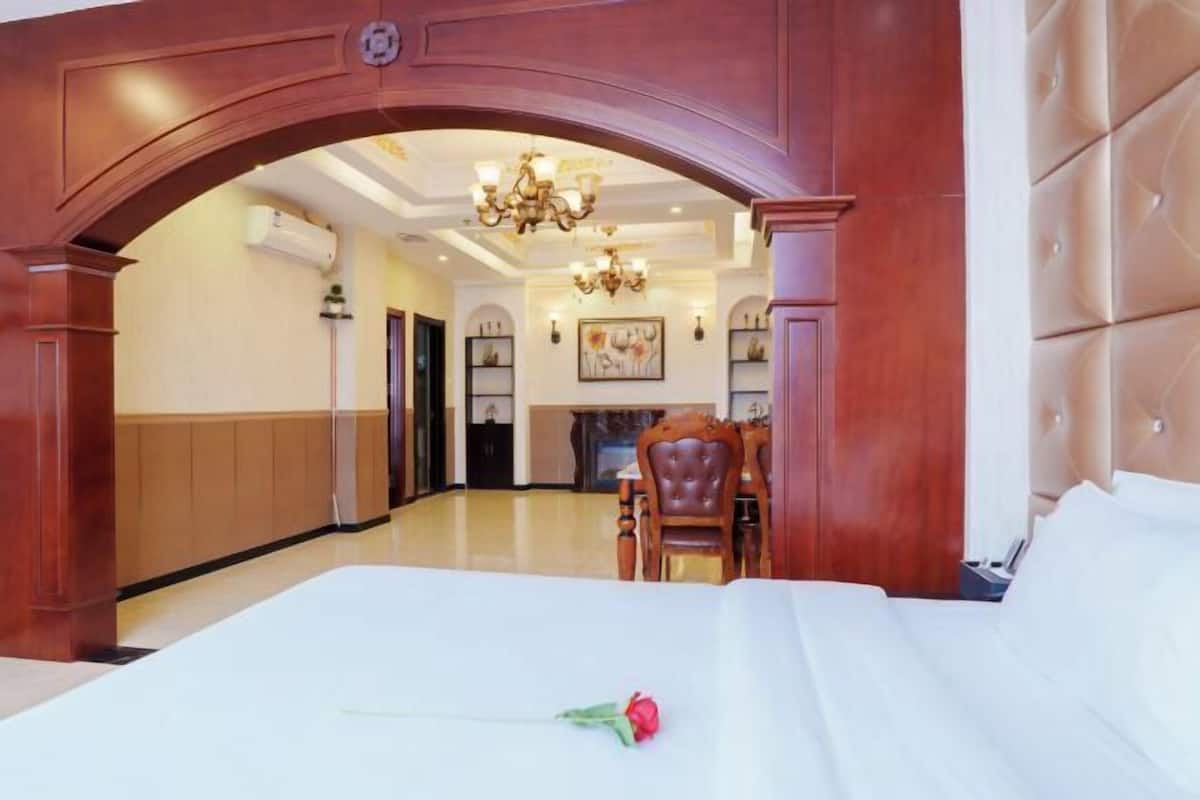 Una habitación de hotel con una cama, un arco de madera, un candelabro y un área de comedor al fondo.