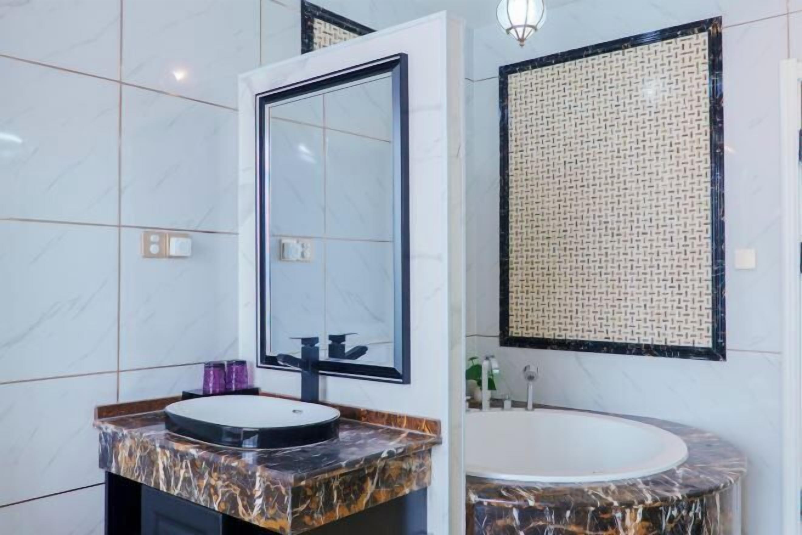 A bathroom with a marble vanity, a large mirror, a round sink, and a bathtub.