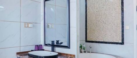 A bathroom with a marble vanity, a large mirror, a round sink, and a bathtub.