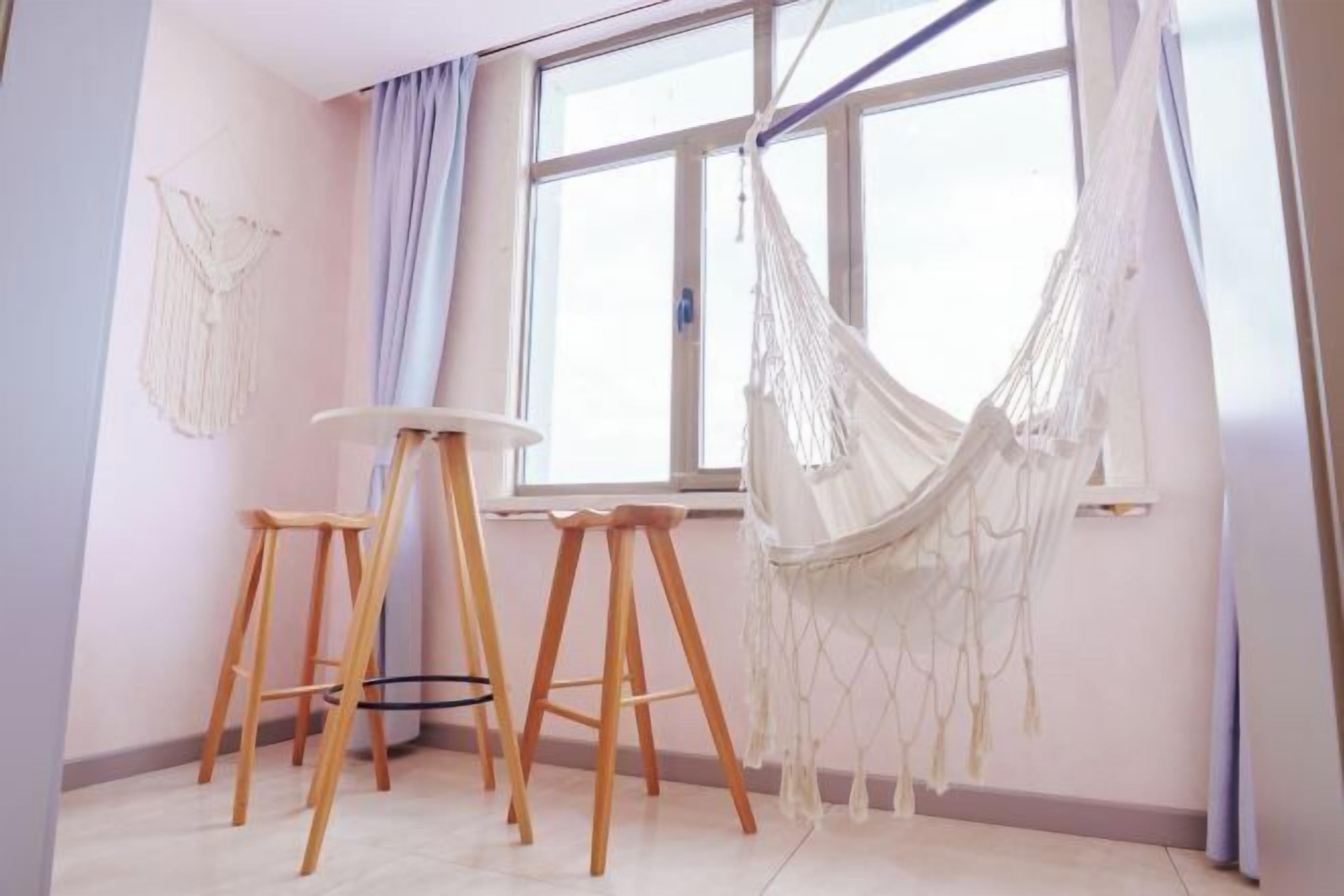 A room with a large window, a hammock, and two wooden stools.