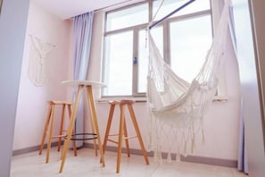 Ein Zimmer mit großem Fenster, einer Hängematte und zwei Holzschemeln.