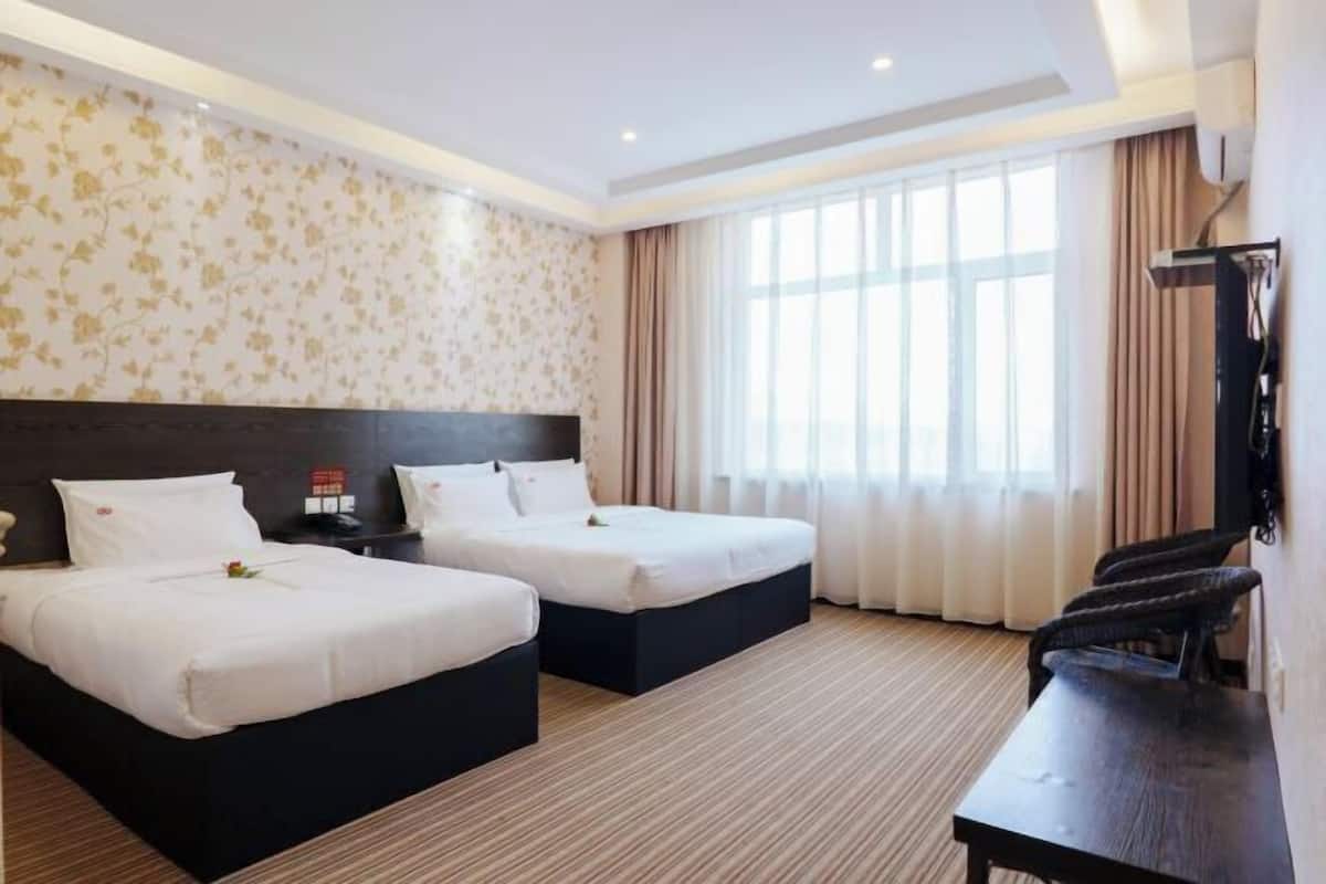 Una habitación de hotel con dos camas, un escritorio, una silla, un televisor y un ventanal grande con cortinas.