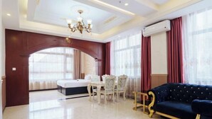 A spacious living room with a dark blue sofa, a white dining table with chairs, a chandelier, and large windows with red curtains. - Hongji Business Hotel (Fujin)