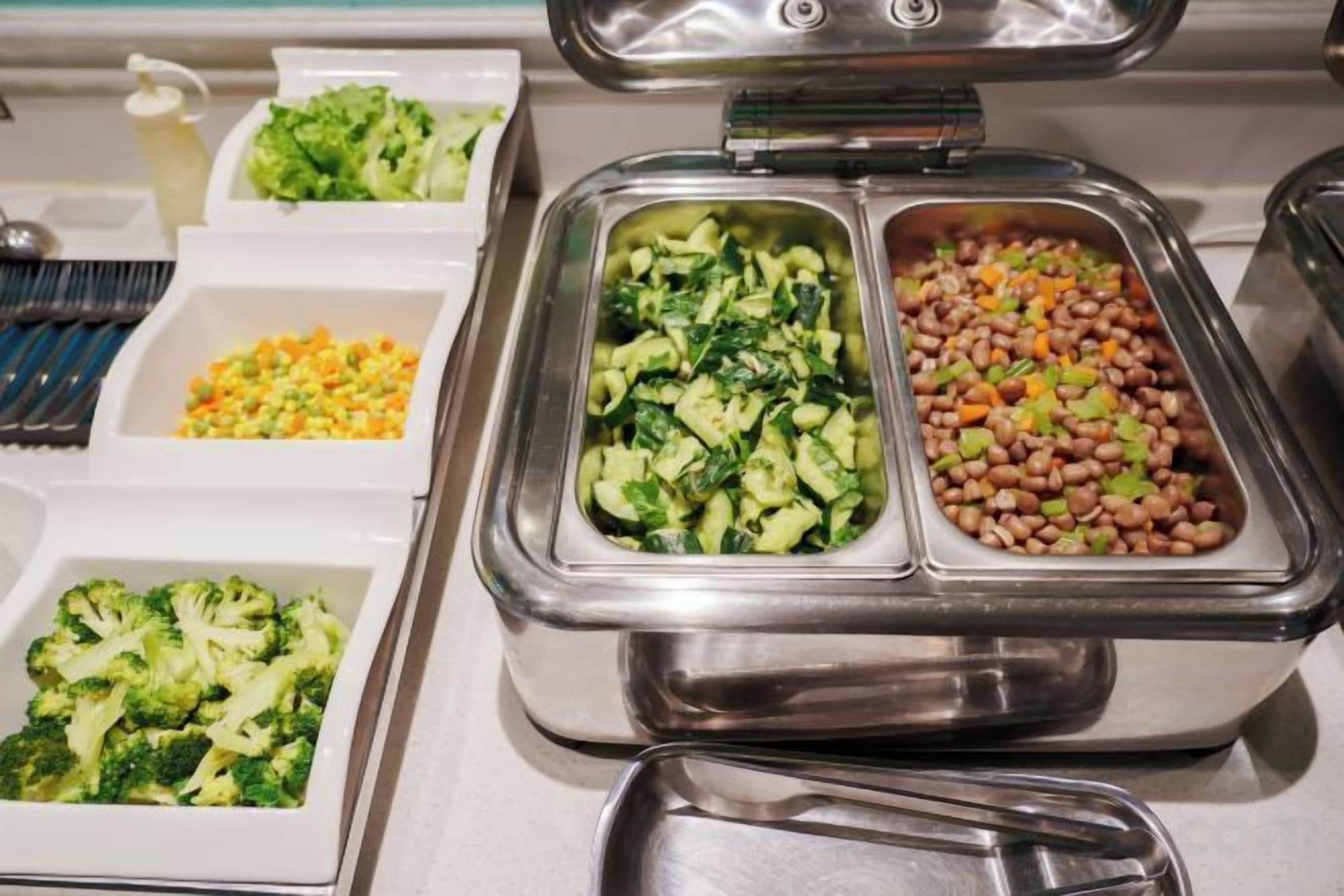 A buffet with various food items including broccoli, beans, and corn.