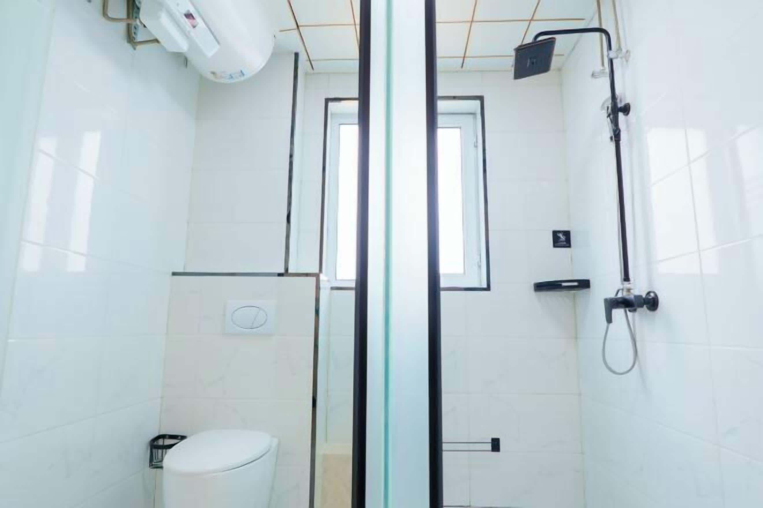 A modern bathroom with a glass shower enclosure, a toilet, and a hand dryer.