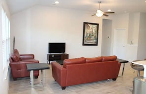 Un salon spacieux avec un canapé en cuir rouge, un téléviseur à écran plat et un ventilateur de plafond.