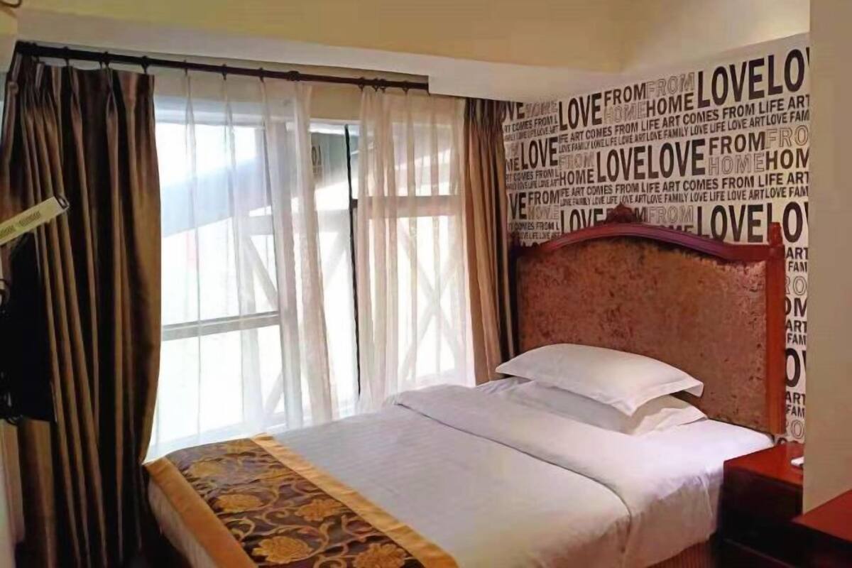 A hotel room with a bed, curtains, a headboard, and a wall with repeated text.