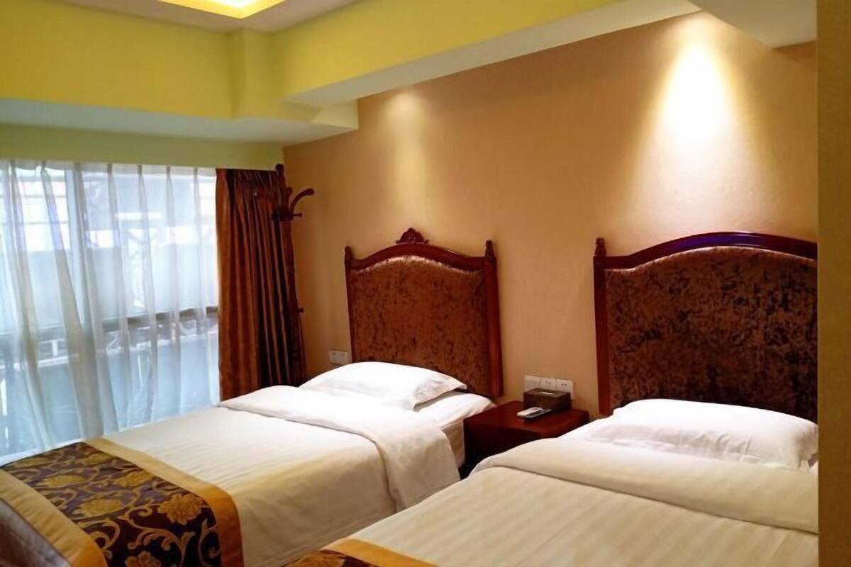 A hotel room with two beds, a wooden headboard, a nightstand, and a window with curtains.