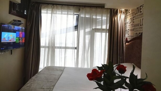 A hotel room with a bed, a TV on the wall, a window with curtains, and a wall with love-themed decorations. - Yi Xiu Hotel (Chongqing)