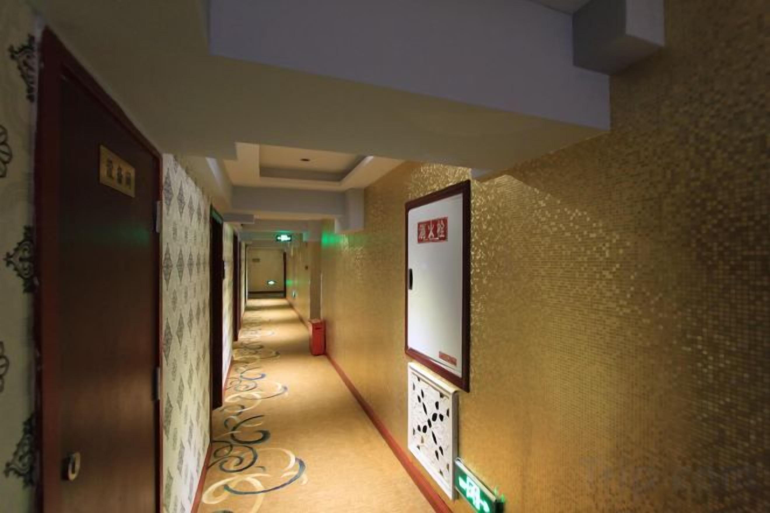 A hotel hallway with patterned carpet, a sign on the wall, and doors on the left.