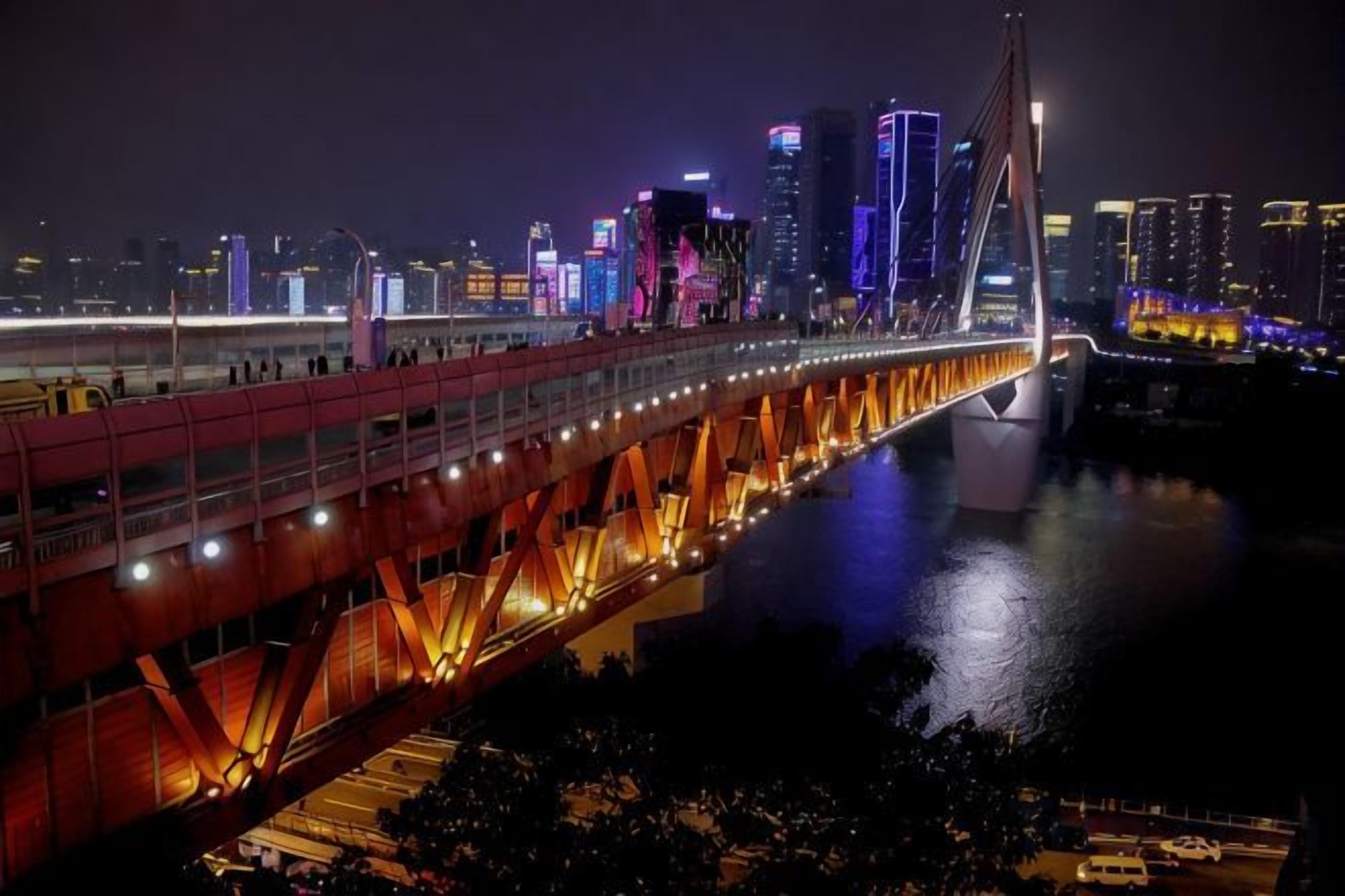 A nighttime cityscape with a prominent illuminated bridge and high-rise buildings.