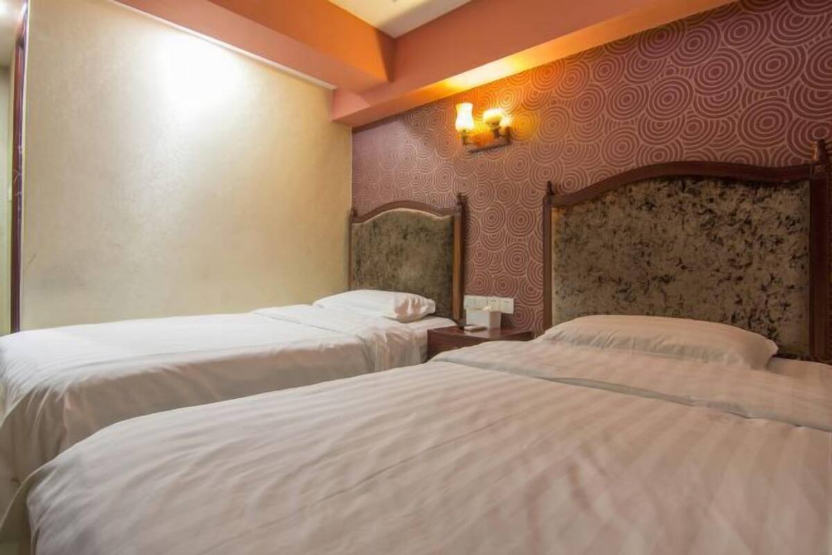 A hotel room with two beds, a headboard with a floral pattern, and a wall-mounted light fixture.