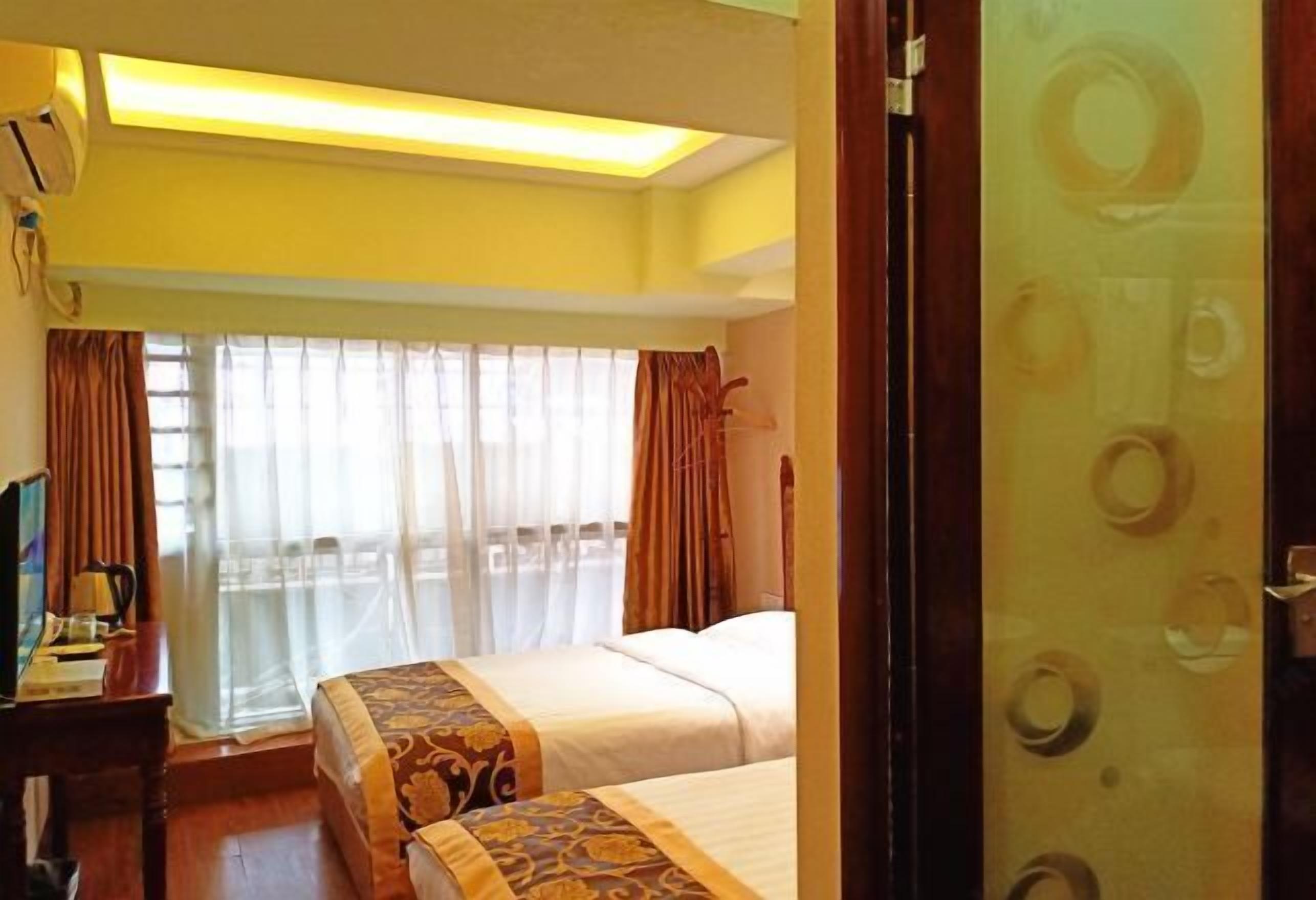 Une chambre d’hôtel avec deux lits, un bureau avec un ordinateur et une fenêtre avec des rideaux.