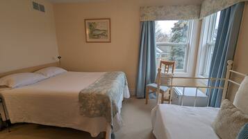 A bedroom with two beds, a chair, a window with curtains, a radiator, and a framed picture on the wall.