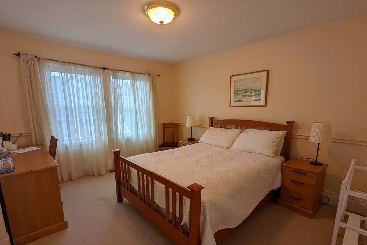 Ein Schlafzimmer mit einem Holzbett, zwei Nachttischen mit Lampen, einem Schreibtisch und einem Stuhl.