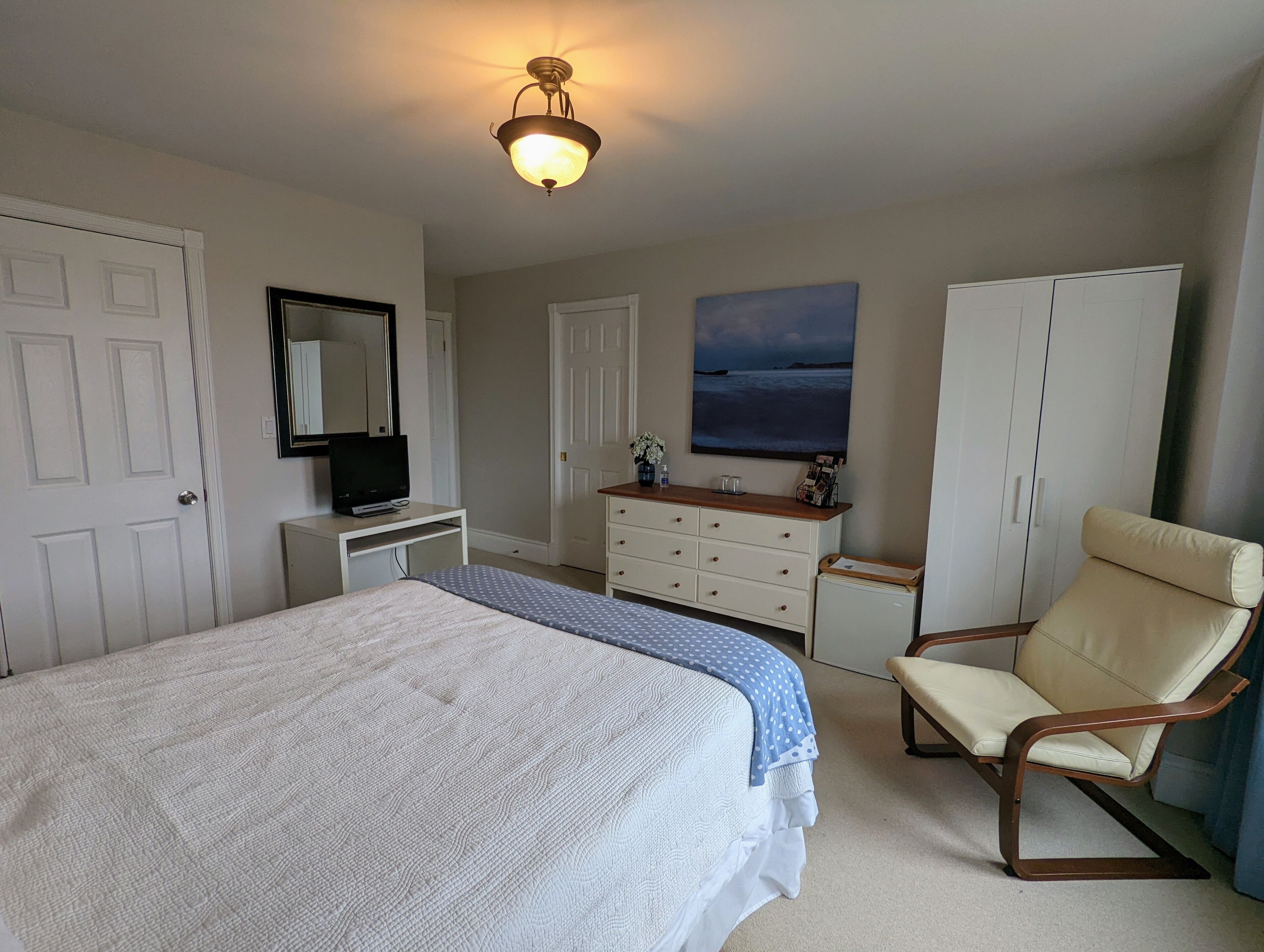 A bedroom with a large bed, a dresser, a chair, a television, and a painting on the wall.