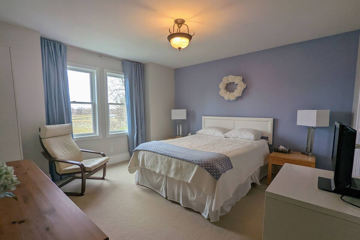 Ein Schlafzimmer mit einem Bett, zwei Nachttischen, einem Sessel, einem Schreibtisch und einem Fernseher.