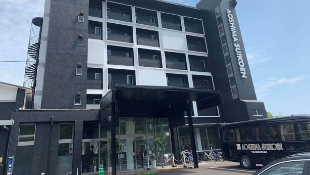 Un bâtiment moderne à la façade noire et blanche, doté d’une grande entrée avec des portes vitrées et d’un espace abrité.