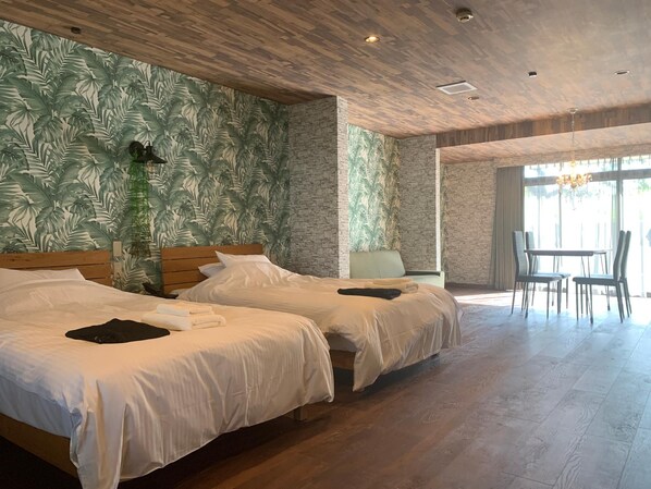 A hotel room with two beds, a dining area with a table and chairs, and a large window. - Aoshima Suikoen Hotel (Miyazaki)