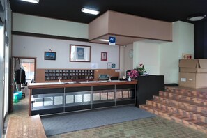 A reception desk with a counter, a clock, framed certificates, and a blue sign indicating a restroom. - Aoshima Suikoen Hotel (Miyazaki)