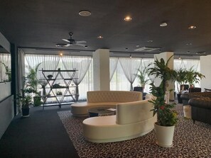 A modern living room with a curved sofa, a coffee table, and a large potted plant. - Aoshima Suikoen Hotel (Miyazaki)