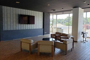 Un hall d’entrée moderne doté d’un espace salon, d’un téléviseur à écran plat fixé au mur et de grandes fenêtres offrant une vue sur l’extérieur.