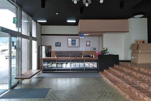 A reception area with a counter, a bench, and a staircase leading to an upper level. - Aoshima Suikoen Hotel (Miyazaki)