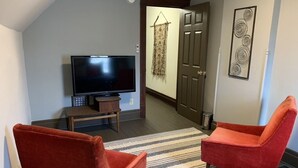 A living room with a flat-screen TV, two red armchairs, a striped rug, and a door leading to another room. - The Red Brick Inn - 10 Minute Walk to the Falls (Niagara Falls)