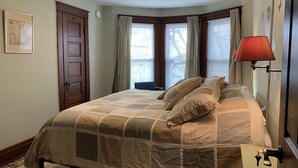 A bedroom with a bed, a door, a window with curtains, and a wall-mounted lamp. - The Red Brick Inn - 10 Minute Walk to the Falls (Niagara Falls)
