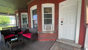 A covered porch with wicker furniture and a red doormat. - The Red Brick Inn - 10 Minute Walk to the Falls (Niagara Falls)
