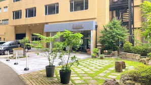 A building with a yellow facade, multiple windows, and a sign with Chinese characters. There are potted plants and a stone pathway in front.