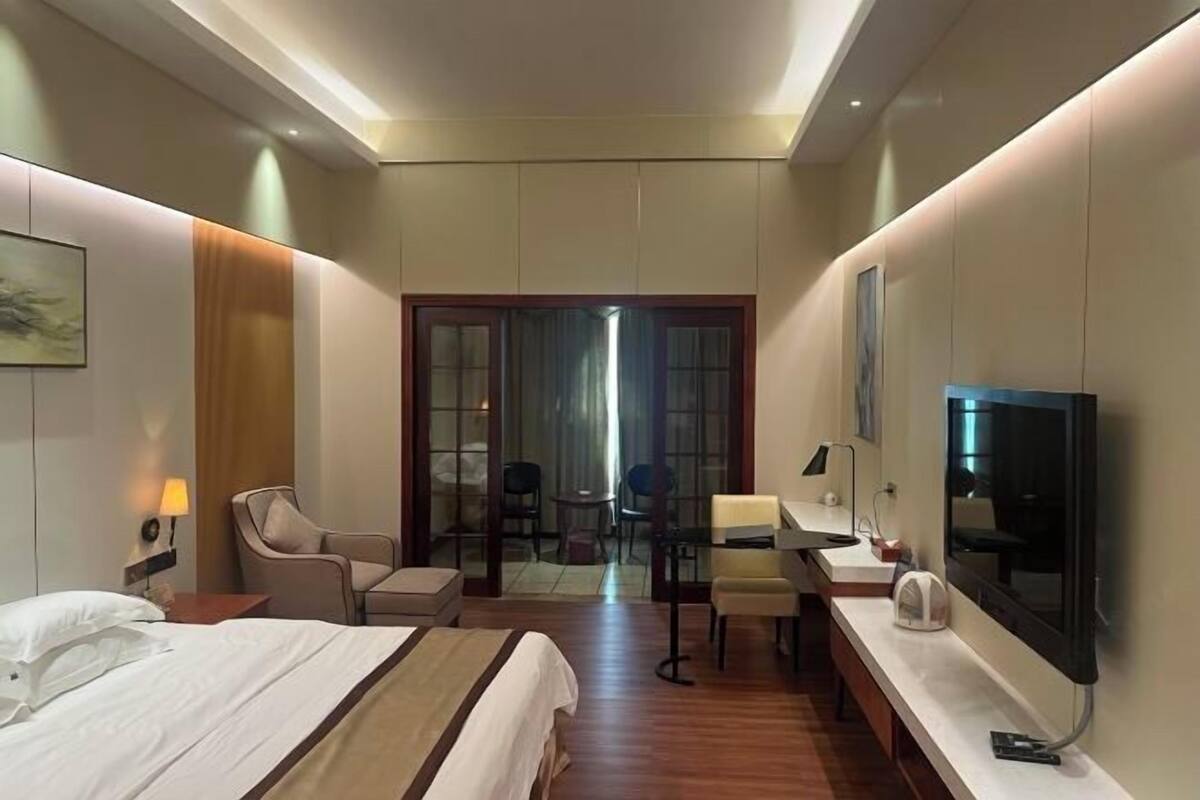 A hotel room with a bed, a desk, a chair, a TV, and a door leading to a balcony.