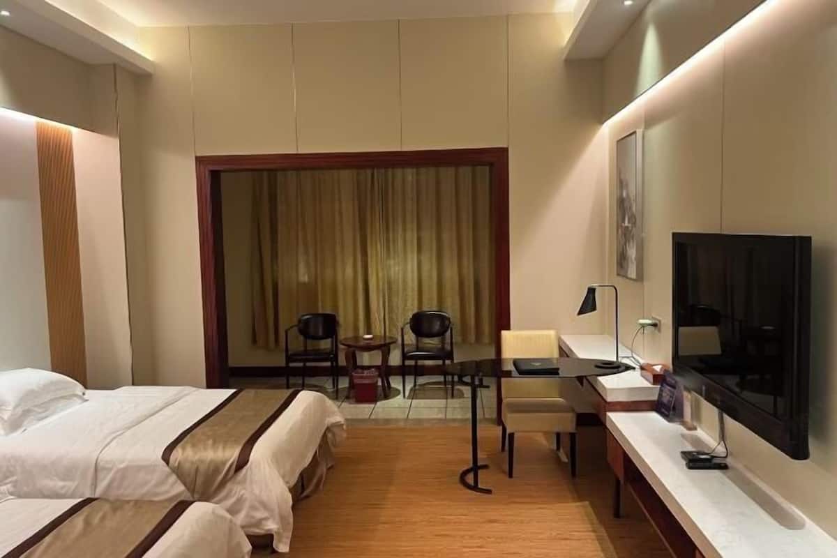 A hotel room with two beds, a desk with a chair, a TV, and a large window with curtains.