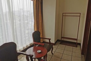 Een hotelkamer met een houten stoel, een klein rond tafeltje en een metalen bijzettafeltje.