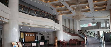 Un vestíbulo amplio con una recepción, una escalera y un candelabro.